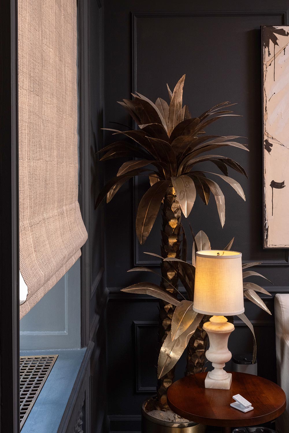 Textured Roman shade in a dark room next to a decorative palm statue
