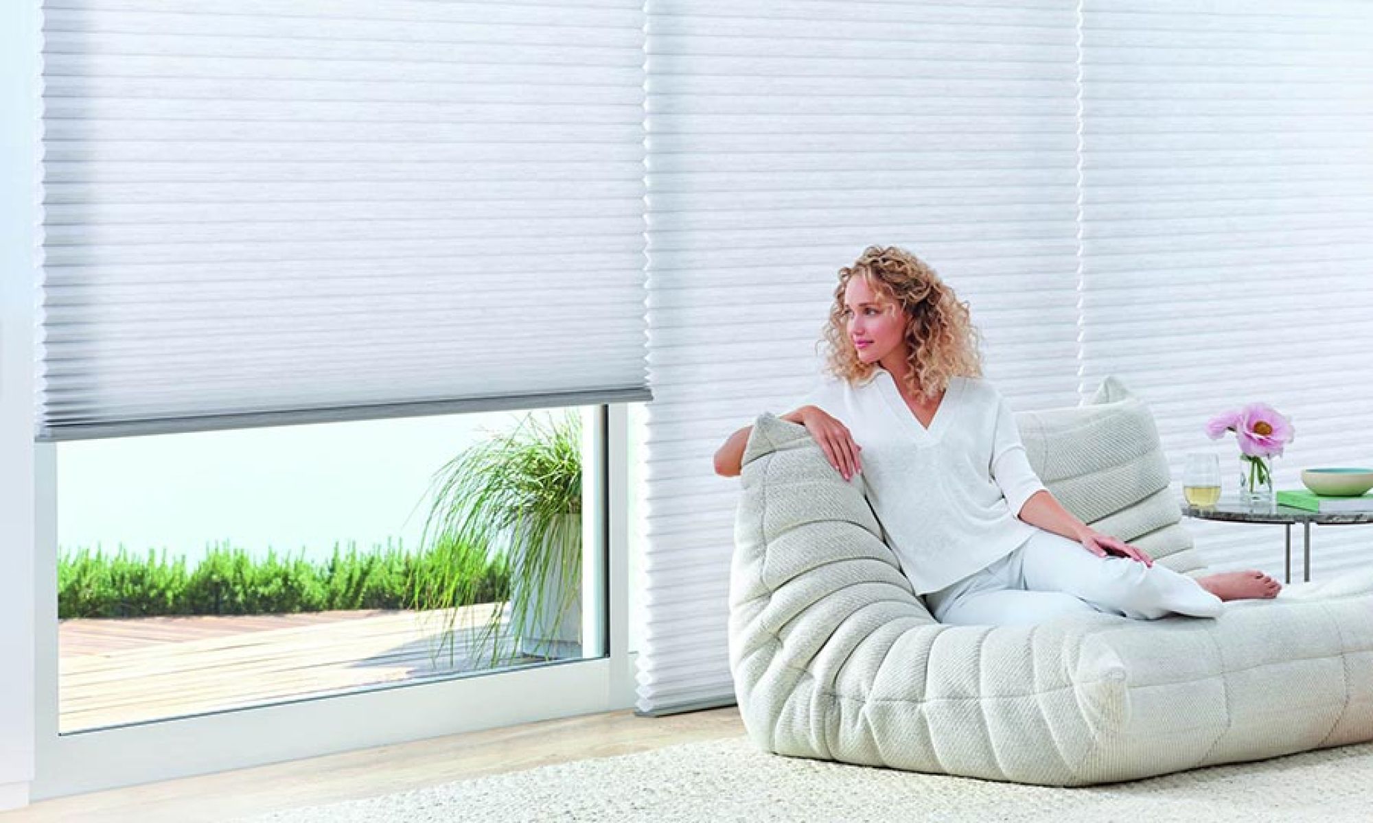 Woman sitting on a modern lounge chair next to large windows with cellular shades